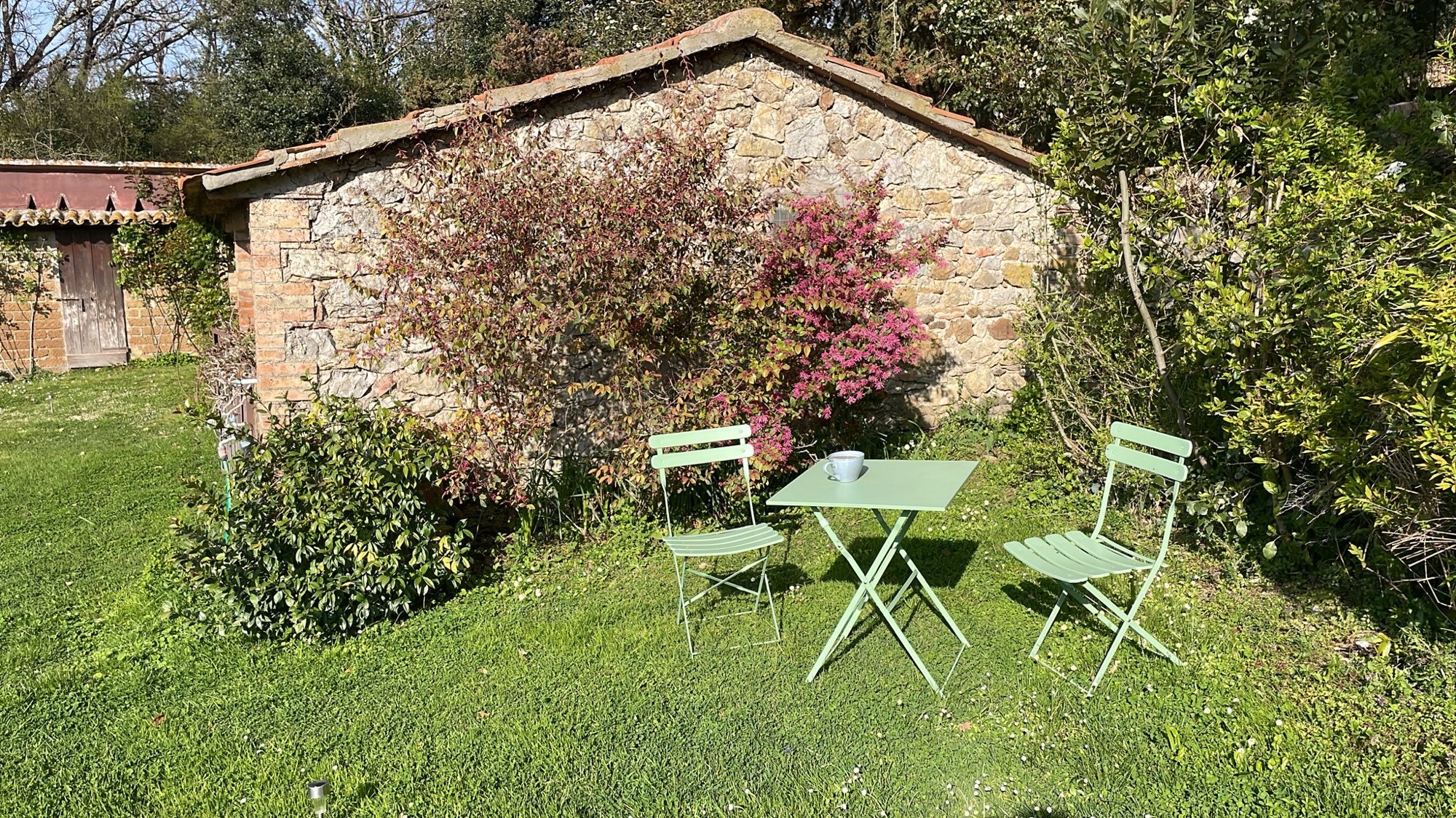 Grüner Bistrotisch mit zwei Stühlen auf der Wiese vor einer Steinmauer